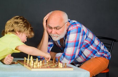 Chess match. Board games. Little boy playing chess with grandfather. Grandpa and grandson playing chess enjoying leisure time. Handsome grandfather and grandson playing chess spending time togetherの写真素材