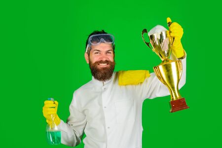 Bearded man in uniform and gloves with cleanser spray and gold trophy cup. Man from professional cleaning service. Domestic work. Cleaning, cleanliness, cleaning products. Housework, housekeepingの写真素材