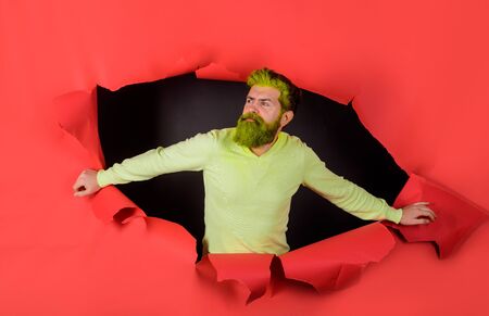 Handsome guy with dyed hair and beard. Fashionable man in yellow sweater. Man looking through hole. Advertising. Discount, sale. Man looking through hole in paper. Bearded man making hole in paperの写真素材