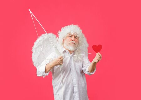 Handsome Cupid. Valentines Day. Angel man with white wings. Love concept. Valentine angel. Bearded man with angel wings. Valentines day card. Cupid holds valnetine's heart. Valentines cupidの写真素材