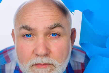 Crying bearded man through hole in blue paper. Copy space for advertising. Discount, sale, season sales. Through paper. Advertising. Close up portraitの写真素材