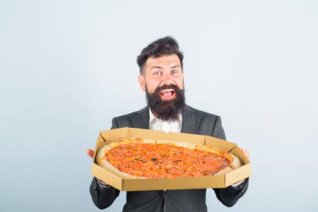 Pizza delivery concept. Food, business lunch. Businessman holds cardboard box with pizza. Taste delicious fastfood. Businessman hold pizza. Delicious italian pizza in box. Bearded businessman in suitの写真素材