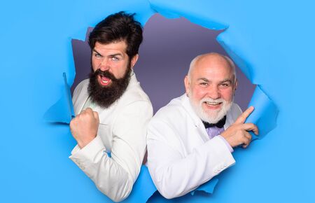 Emotions. Men making hole in paper. Advertising. Success. Successful men look through hole in paper. Bearded men peeking from ripped paper hole. Discount. Sale. Season sale. Copy space. Through paperの写真素材