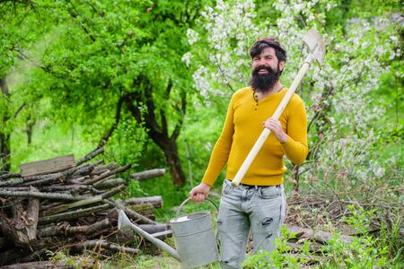 Watering. Gardening. Farm. Gardener work. Farmer working in garden. Work in garden. Spring. Smiling man preparing to planting. Plants. Bearded gardener with garden watering can and spadeの写真素材