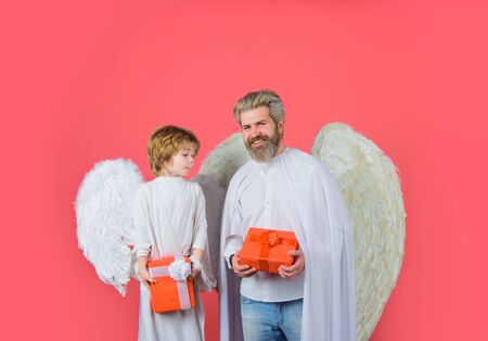 Valentines day. Little cupid boy gives father gift. Father's day. Gift box. Happy father in angel costume with little son angel holds present. Cute angel. Father and son Angels. Christmas angelsの写真素材