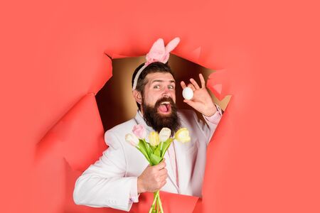 Easter Day. Happy bearded man holds easter egg and flowers. Spring holiday. Easter bunny costume....