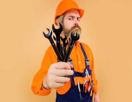Wrenches. Repairment tools. Worker holds wrenches. Building. Industry. Technology. Spanner. Bearded builder. Builder in construction helmet. Hard hat. Selective focusの写真素材