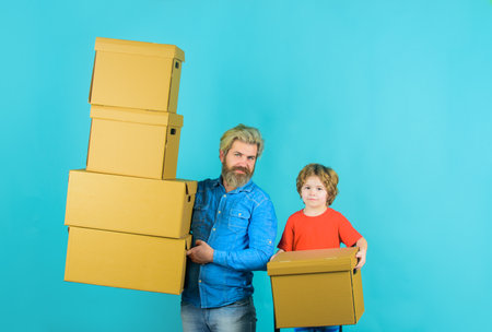 Moving, home and family concept. Father and son holds cardboard boxes. Father holds stack cardboard boxes and son helping him. Prepare for moving. Father and son with shipping boxes. Packaging thingsの写真素材