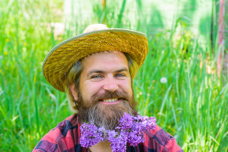 Lilac. Spring. Bearded man with flowers in beard. Hipster beard with flowers. Barber shop advertising. Beard style. Outdoorの写真素材