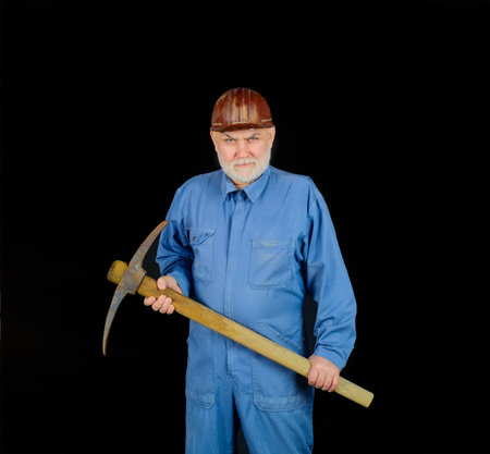 Man holding pick-ax. Male miner worker in coveralls with pickaxe. Construction and building works. Bearded man in uniform holds pick ax. Builder man holds pickaxe. Craftsman working with pickaxeの写真素材