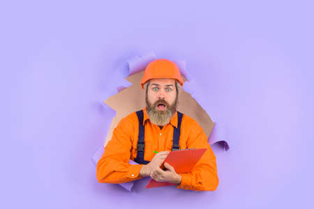 Through paper. Advertising. Repair. Building concept. Engineer making notes. Surprised repairman with folder. Construction worker with folder. Repairman with folder. Man in hard hat. Helmetの写真素材