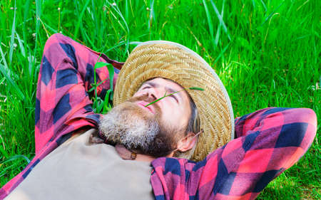 Man lying on grass. Happy relaxed male in checkered shirt and hat. Guy relaxing outdoors in summer. Enjoying sunny day. Unity with nature.の写真素材
