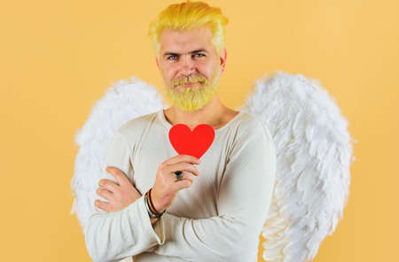 Happy Valentine Day. Male angel with red heart. Bearded man with white wings holds paper heart.の写真素材