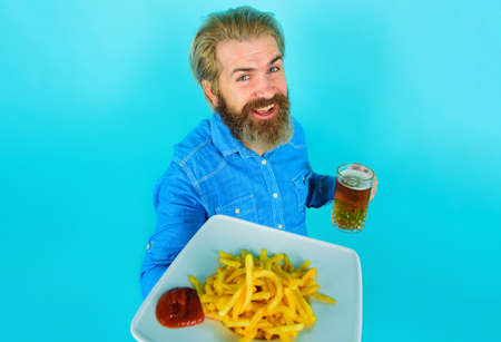Smiling Man with potato fries and beer. French fries potato. Bearded Male with Potatoes fries and ketchup on plate.の写真素材