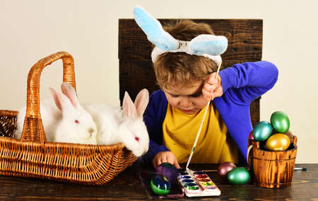 Little boy with easters rabbit in basket. Child in bunny ears paint Easter egg.
