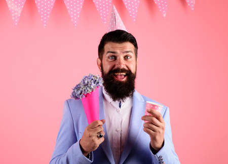 Birthday celebration. Smiling bearded man in party hat with bouquet flowers.の写真素材