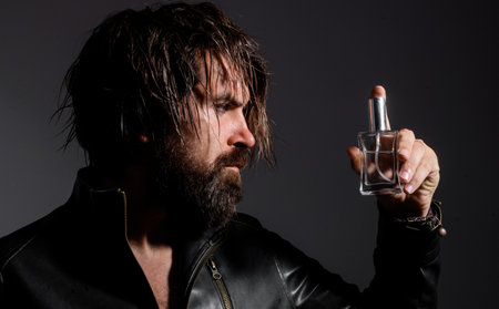 Bearded man in leather jacket with Bottle of perfume or cologne. Cosmetics advertising.の写真素材
