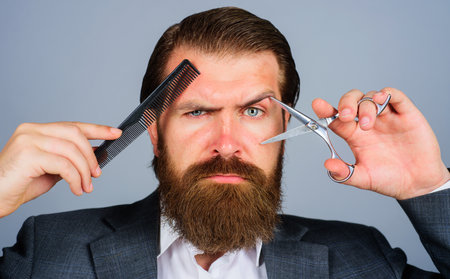 Bearded man with Scissors and comb. Hairdresser with barber tools. Male stylist in barber shop. Beauty and hair salon.の写真素材