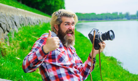 Bearded man taking photo with camera on river. Hobby and travel. Smiling man with professional...
