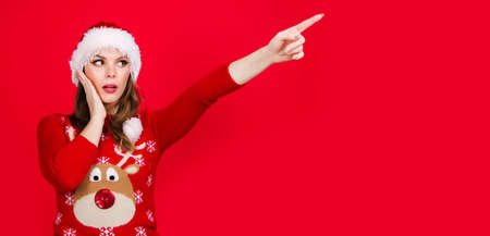 New year advertising. Christmas woman pointing finger away at copy space. Surprised girl in Santa hat. Season Sales and discount.の写真素材