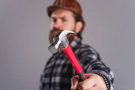 Worker, Carpenter or builder in hard hat with hammer. Selective focus. Bearded man in helmet hammering nail.の写真素材