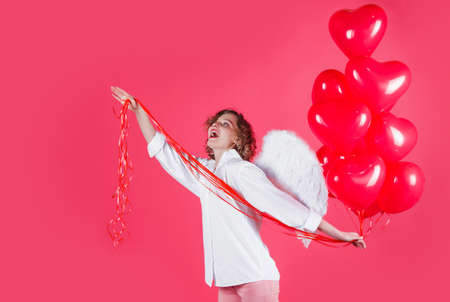 Valentines day. Angel woman with heart shape balloons. Happy girl with white wings. Copy space.の写真素材