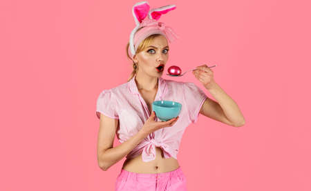 Easter Day. Woman with pink egg on spoon. Surprised girl in bunny ears. Coloring eggs. Hunting eggs.の写真素材