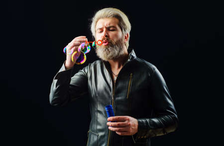 Handsome man blowing bubbles. Play with Soap bubble. Bearded guy in leather jacket. Good mood.