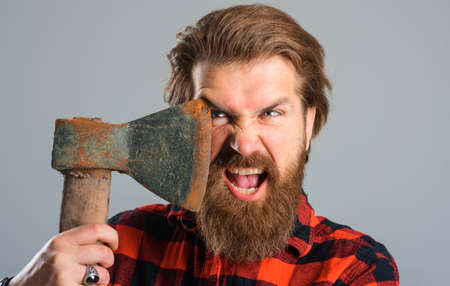 Angry bearded man with axe near face. Brutal Canadian lumberjack with old ax. Closeup.の写真素材