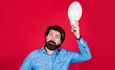 Confused man with with light bulb. Bearded man with big lamp. Lightbulb in hand. Energy, electricity.の写真素材