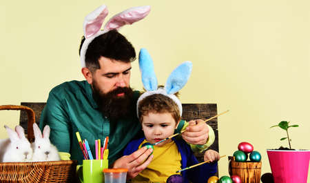 Father and son enjoy painting Easter eggs. Happy family in bunny ears preparing for holiday.