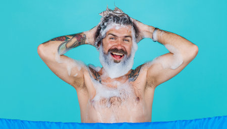 Happy bearded man washing hair with anti-dandruff shampoo. taking shower. Morning routine procedureの写真素材