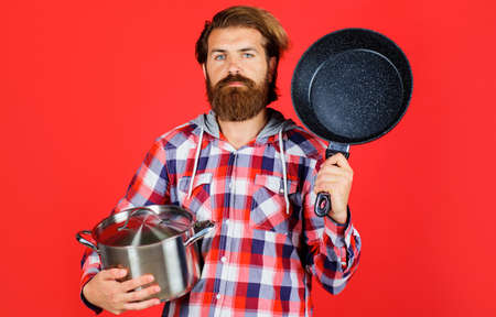 Serious bearded man with frying pan and saucepan. Cooking utensils. Guy with frypan and pot. Kitchen