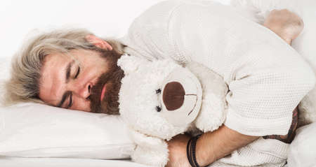 Bearded man sleeping in comfortable bed with teddy bear. sweet dreams. weekend morningの写真素材