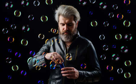 Bearded man blowing Soap bubbles. Handsome guy in leather jacket having fun playing with bubbleの写真素材