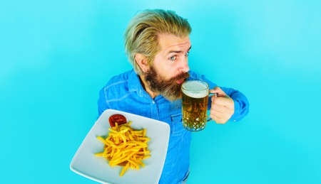 Bearded man eating potato fries and drinking beer. Fried potatoes and ketchup on plate. fast foodの写真素材