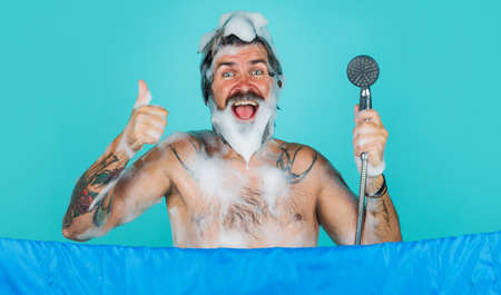 Bearded man with foam on head taking shower showing thumb up. Body washing in the bathroom. hair...