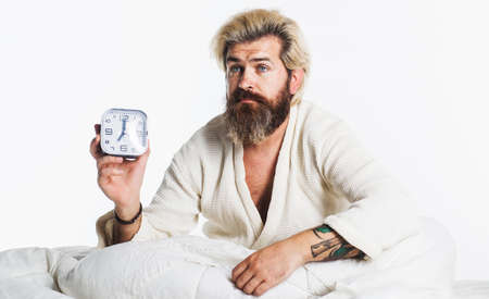 Sleepy bearded man with alarm clock in bed. Morning time. Awakingの写真素材