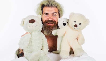 Smiling man with teddy bears in bed. Bearded guy with plush toys. Good morning. sleeping toyの写真素材