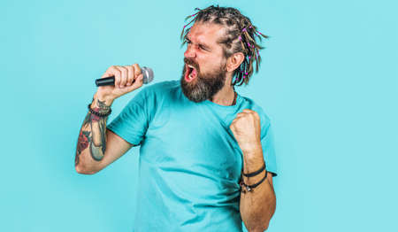 Karaoke. Bearded man singing in microphone. Emotional singer with braids. Sing a song in studioの写真素材