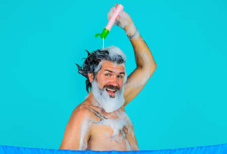 Smiling bearded man pouring shampoo on head. male haircare. washing hair. taking shower. bath timeの写真素材