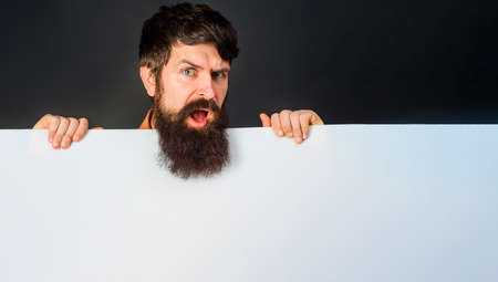 Confused bearded man with advertising banner. Handsome guy shows empty board with space for textの写真素材