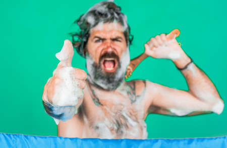 Bearded man soaped with foam washes in shower shows thumb up gesture. body washing. haircare. spa