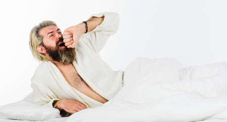 Handsome bearded man in the morning yawning and stretching in bed. Sleepy guy in bathrobe. Awakingの写真素材