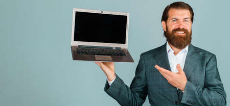 Smiling businessman shows with hand at laptop. bearded man with computer. Blank screen on notebookの写真素材