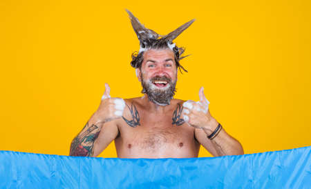 Bearded man taking shower shows thumbs up. Male with foam on head. haircare. bathing. Showering