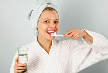 Smiling woman brushing teeth in bathroom. Morning. Happy girl with toothbrush and glass waterの写真素材