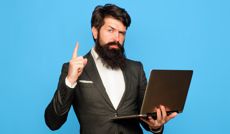Bearded man with laptop computer pointing finger up. Businessman with notebook in office.の写真素材