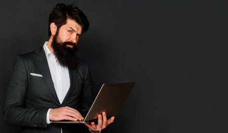 Serious man with laptop computer. Businessman works with notebook in office. Technology and internet.の写真素材