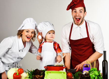Homemade food. Family preparing dinner in kitchen. Little son and parents in uniform and chef hat.の写真素材